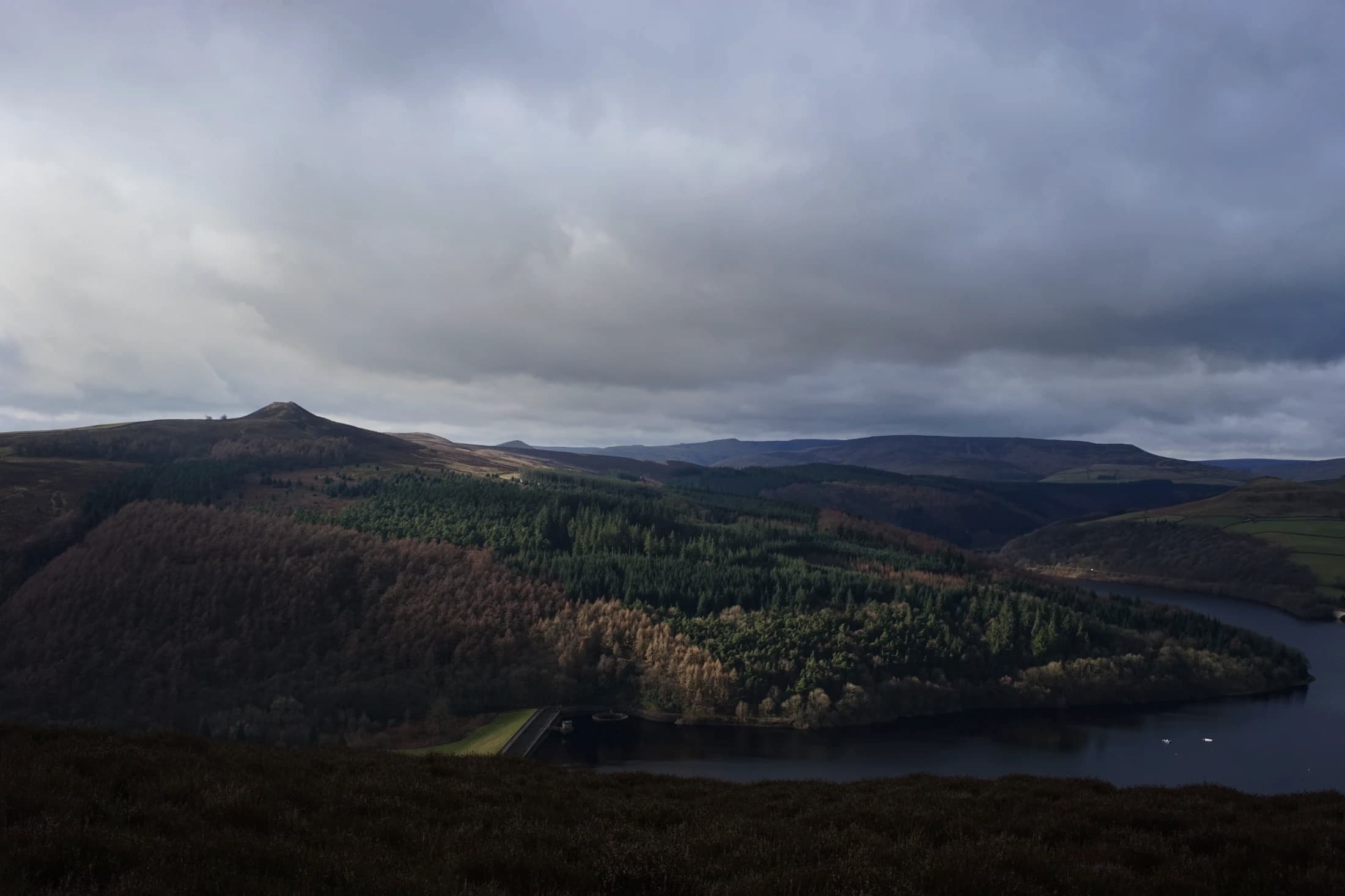 Reservoir and wooded hills beneath an overcast sky