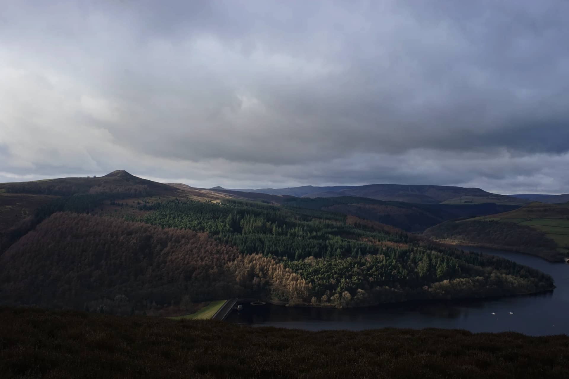 Reservoir and wooded hills beneath an overcast sky